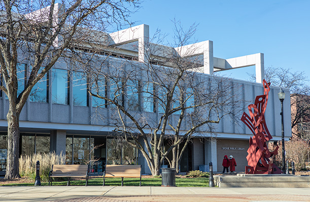 The east exterior of the Skokie Public Library on a sunny day, showing a large red sculpture outside, trees, and a row of second floor windows. The east exterior of the Skokie Public Library on a sunny day, showing a large red sculpture outside, trees, and a row of second floor windows.