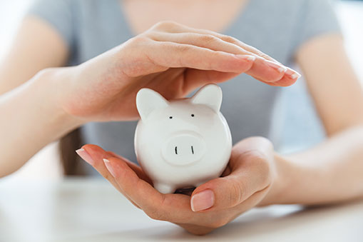 A person holding a small white piggy bank in one hand while hovering the other hand just above it.