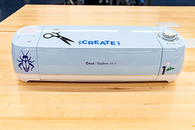Cricut Vinyl Cutter machine sitting on a wooden desk covered in a few stickers