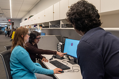 three library staff members huddled around a computer.