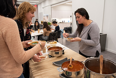 Women standing of a potluck table smiling, eating, and talking