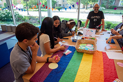 Teens gathered at a table with a pride flag on it.