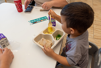 A child seated at a table eating a box lunch