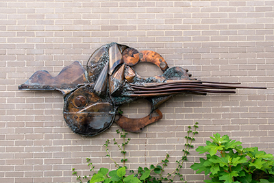 metal sculpture mounted on the outside of a brick wall