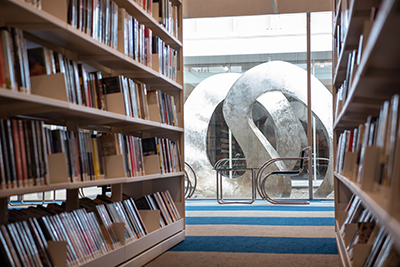 Standing in the library between two bookcases looking out the glass windows towards the metal sculpture