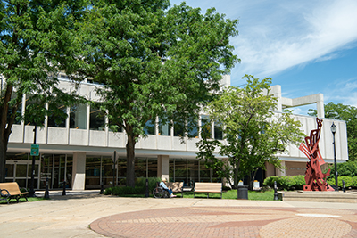 Front of a library building with benches, sculptures, and trees out front