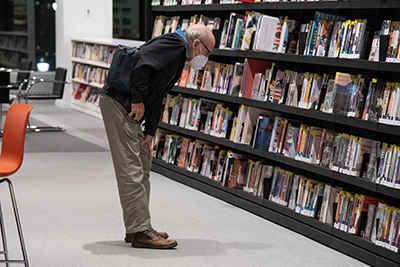 A patronn wearing a face mask and browsing the shelves in the library