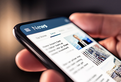 Hand holding a phone that displays a news page.