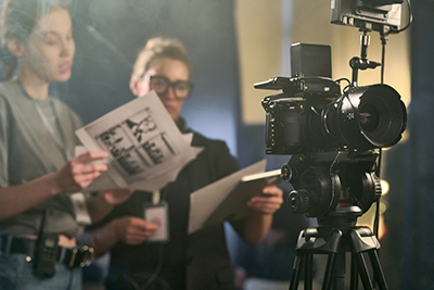 Two women directors standing behind a camera and looking at scripts