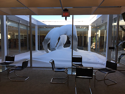 Looking out glass windows towards a large metal sculpture of swans covered in snow