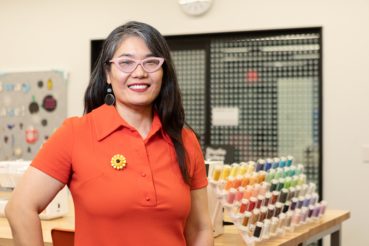 maker in residence, Julie Oh smiling while standing in front of a thread station