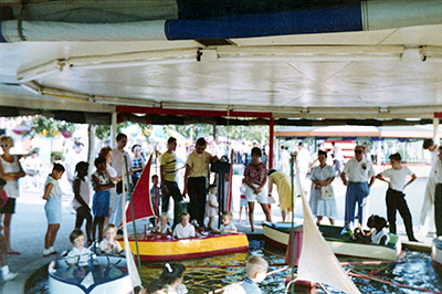A carousel of kiddie boats and parents surrounding it watching