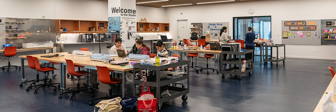 Studio header showing a group of four people working at one table and two others standing at another table