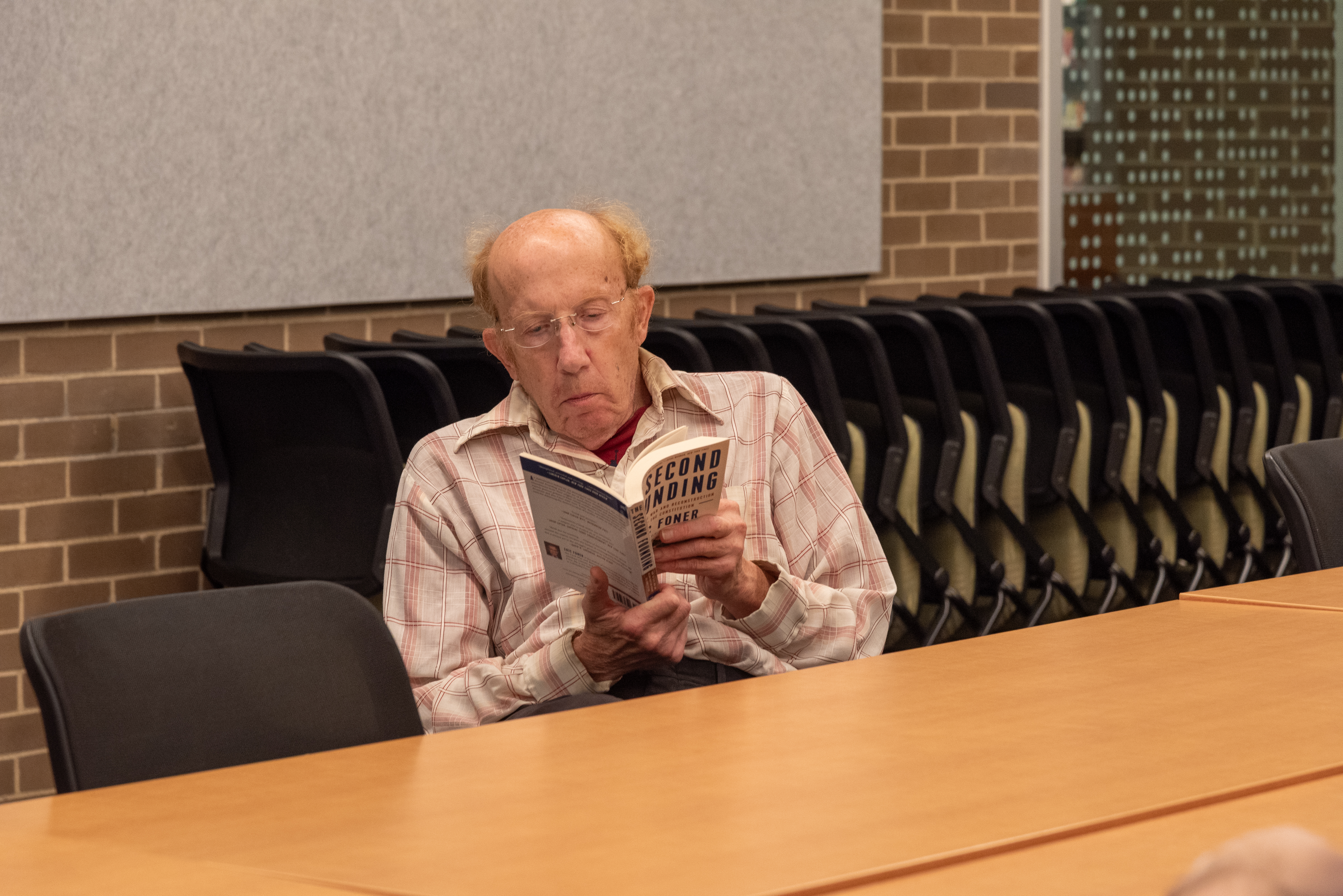 older man seated while holding open a book. 