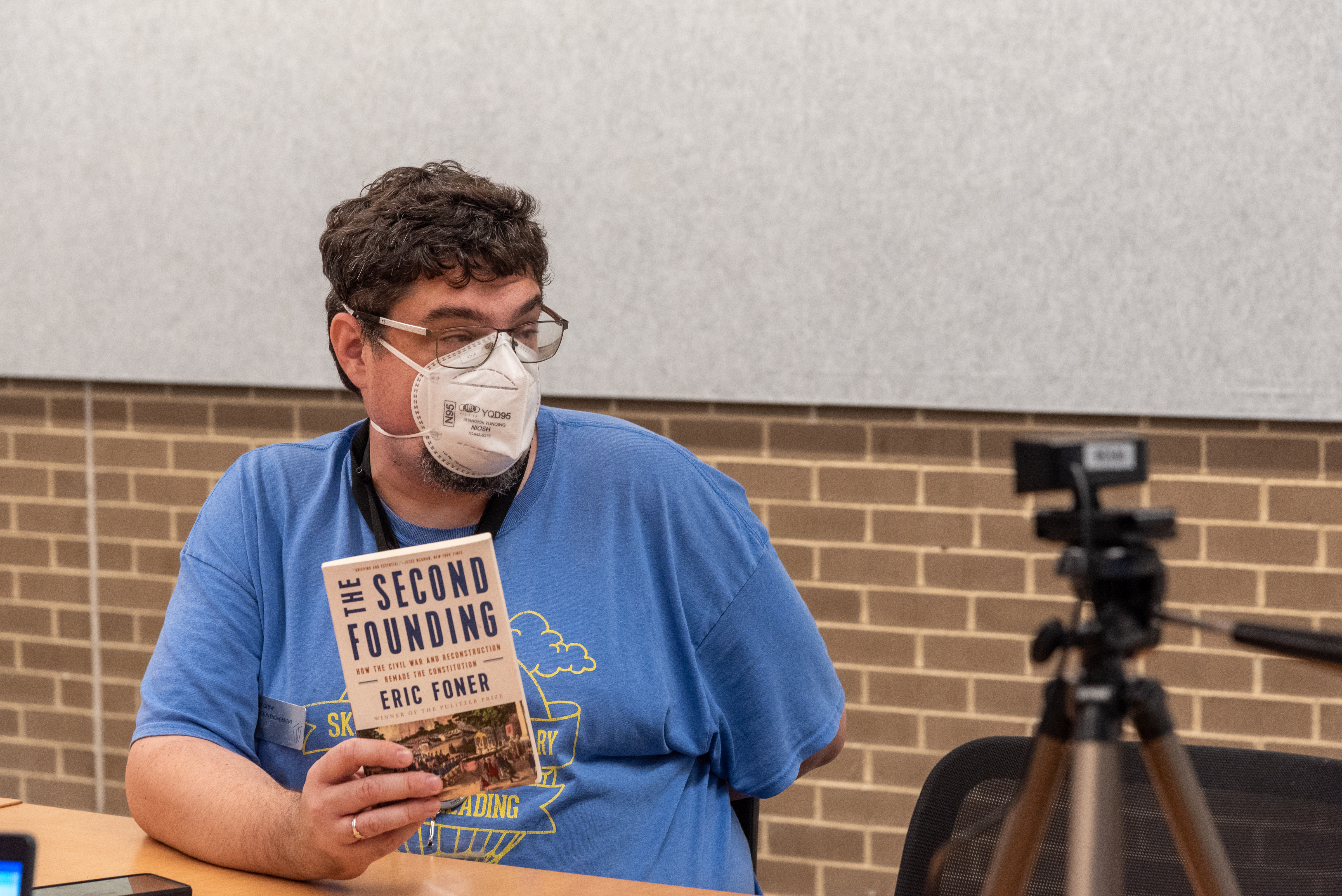 A staff member holding up a book while speaking into a camera