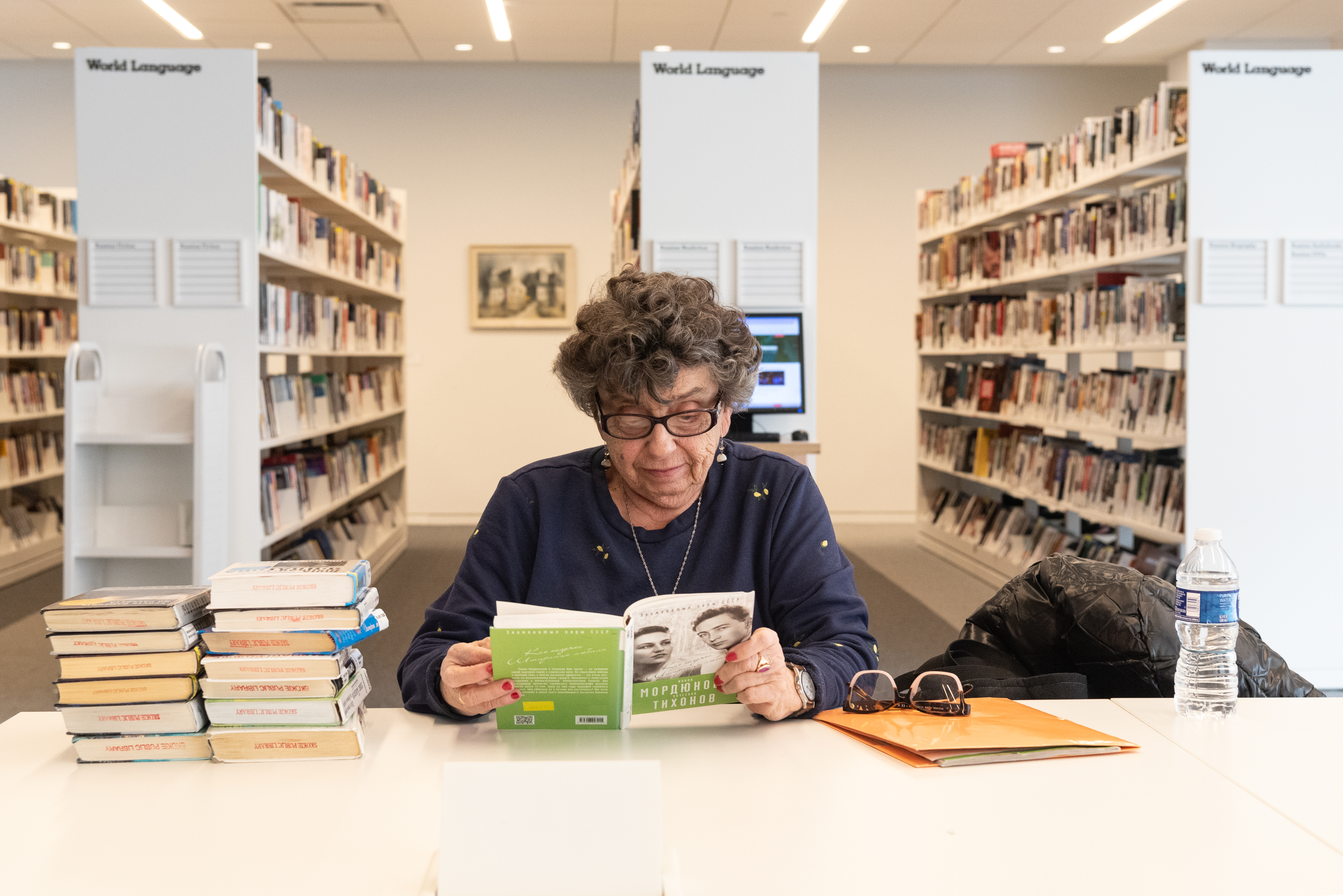 an older woman is looking down at a book in Russian. 