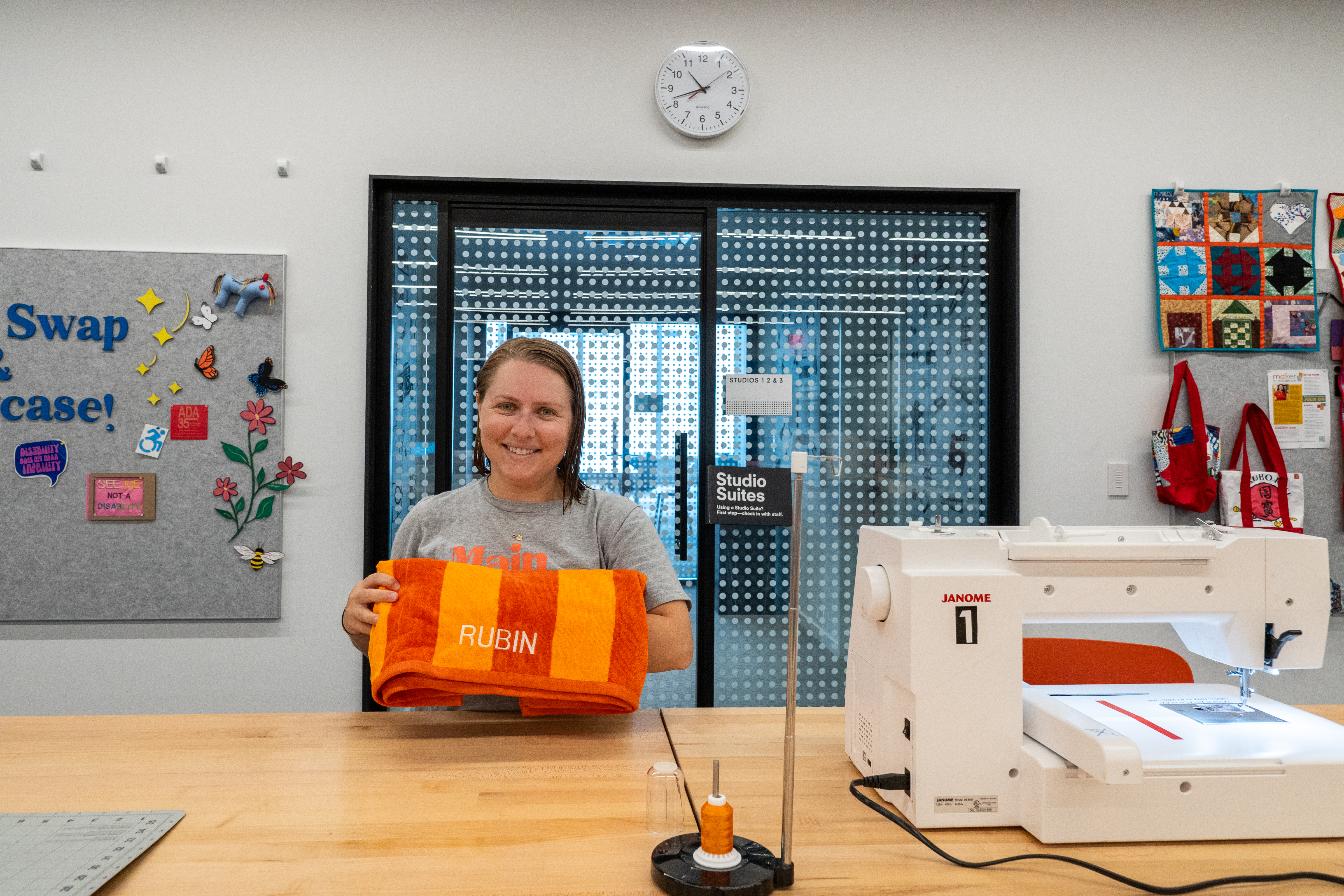 woman standing next to an embroidery machine in the Studio holding an orange towel with "Rubin" embroidered on it.