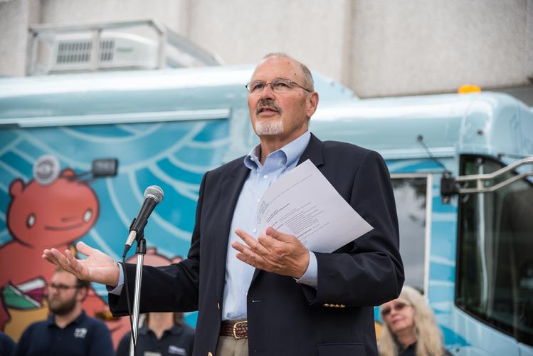 A man speaking into a microphone while standing in front of the bookmobile