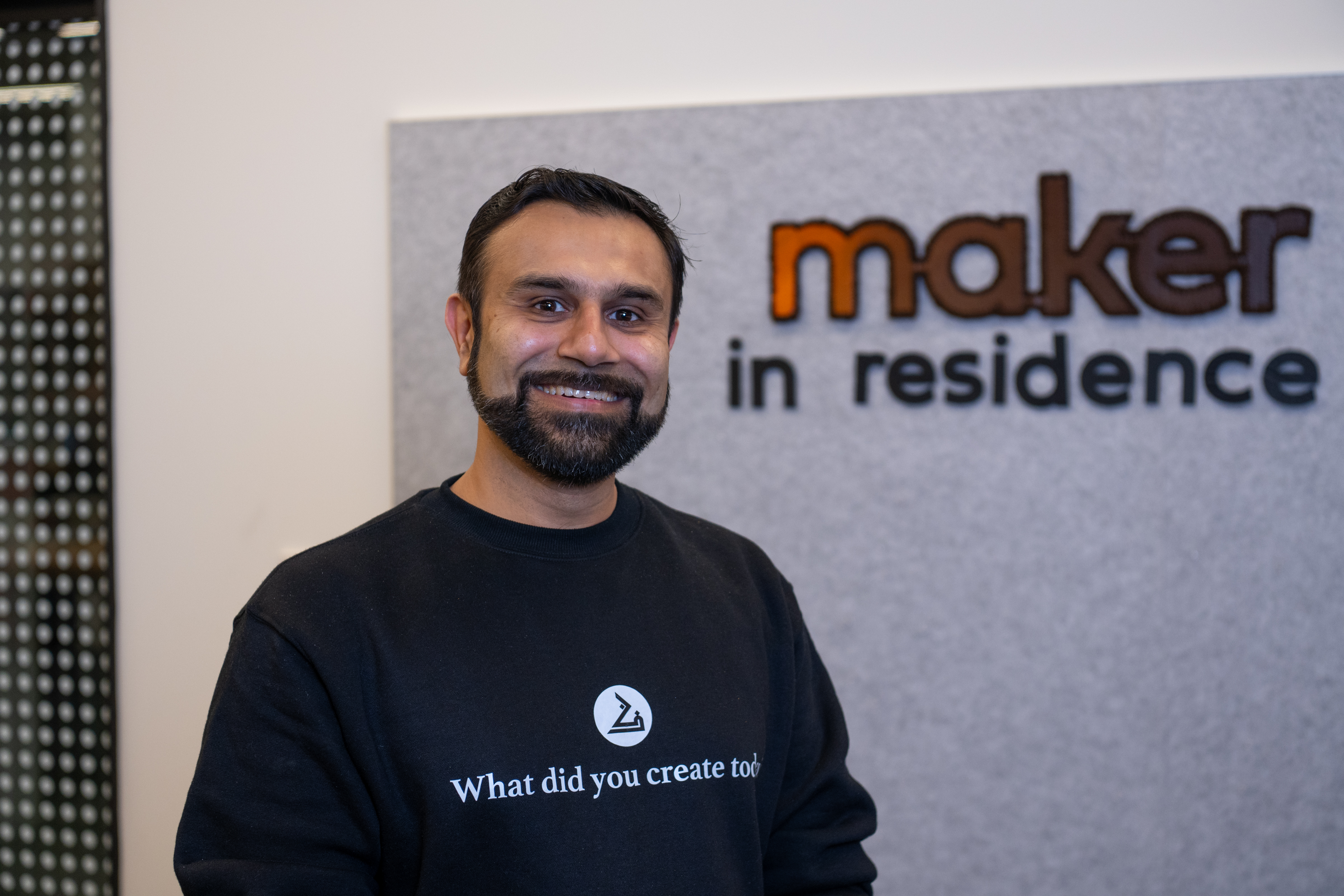 headshot of Zeeshan Farooq smiling. A sign behind him reads "maker in residence" 
