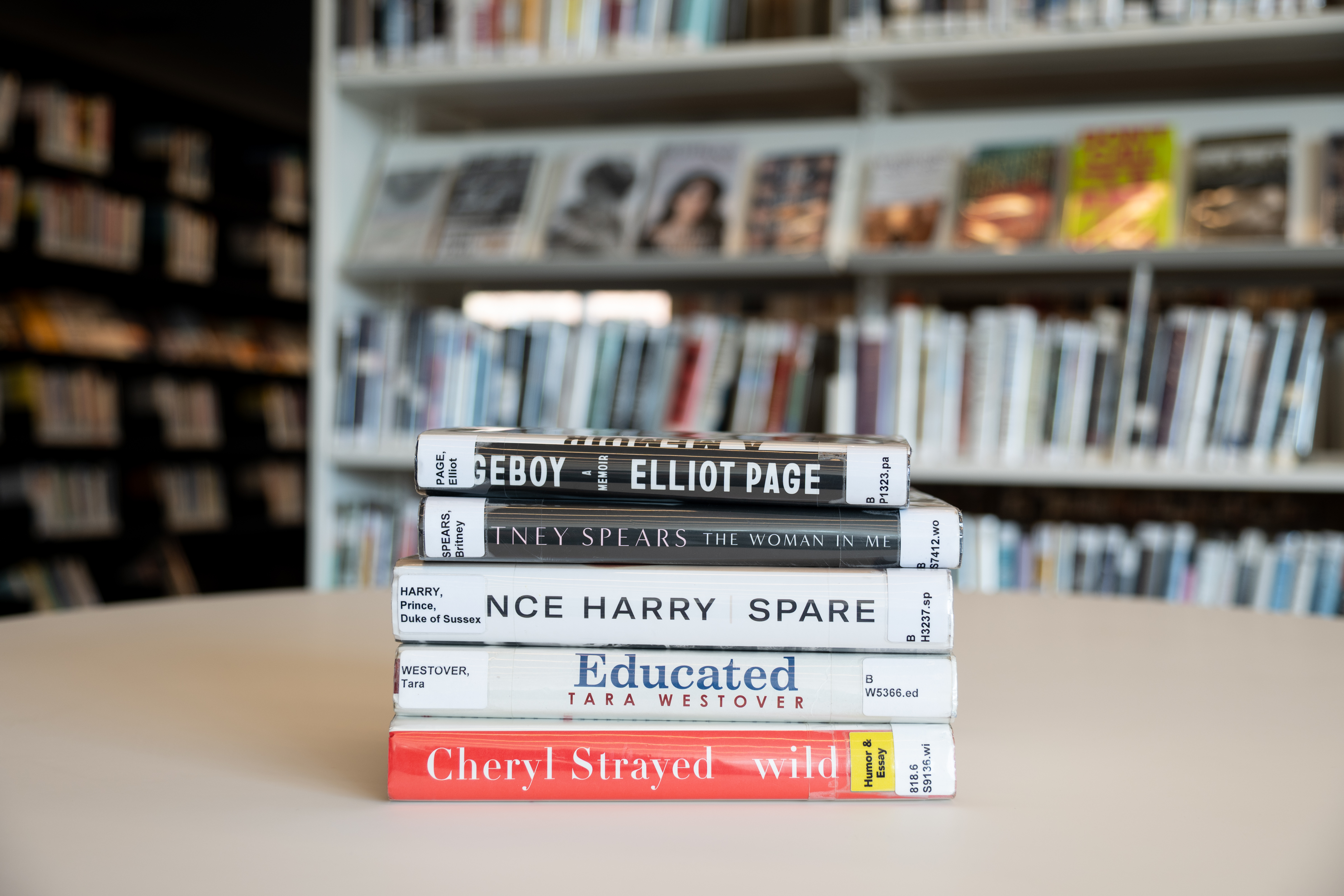 stack of memoirs on a table. There are shelves of books in the background. 