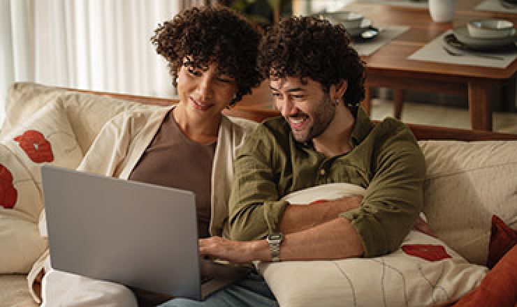 two adults sitting together on a couch and looking down at a laptop