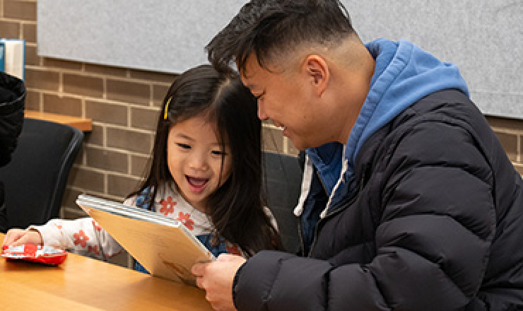 an adult man sitting at a table and reading with a young girl