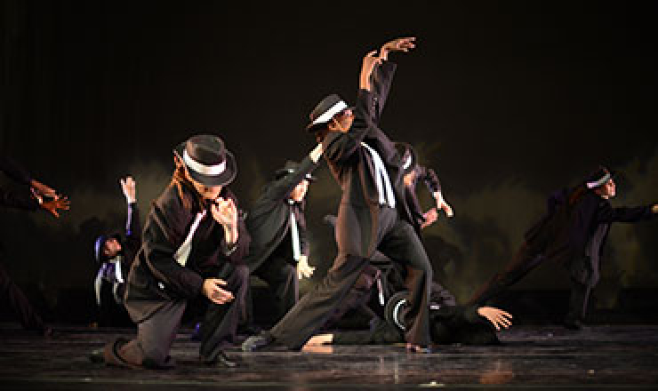 people where black suits in different dance positions on a stage. 