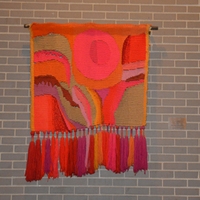 Wool wall hanging is composed of bright pinks and reds with pale orange, olive green, and yellow.