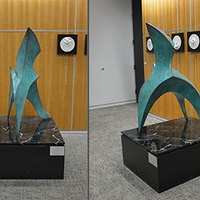 Arched, abstract, three-legged sculpture with curved, angled, pointed top. Bronze with green patina on a custom marble base.