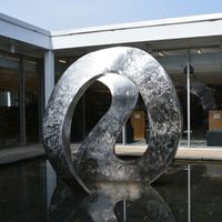 Sculpture of a continuous curved piece of polished and burnished stainless steel with a double loop effect reminiscent of swimming swans.