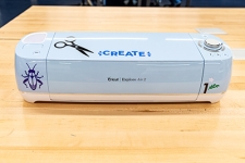 Cricut Vinyl Cutter machine sitting on a wooden desk covered in a few stickers